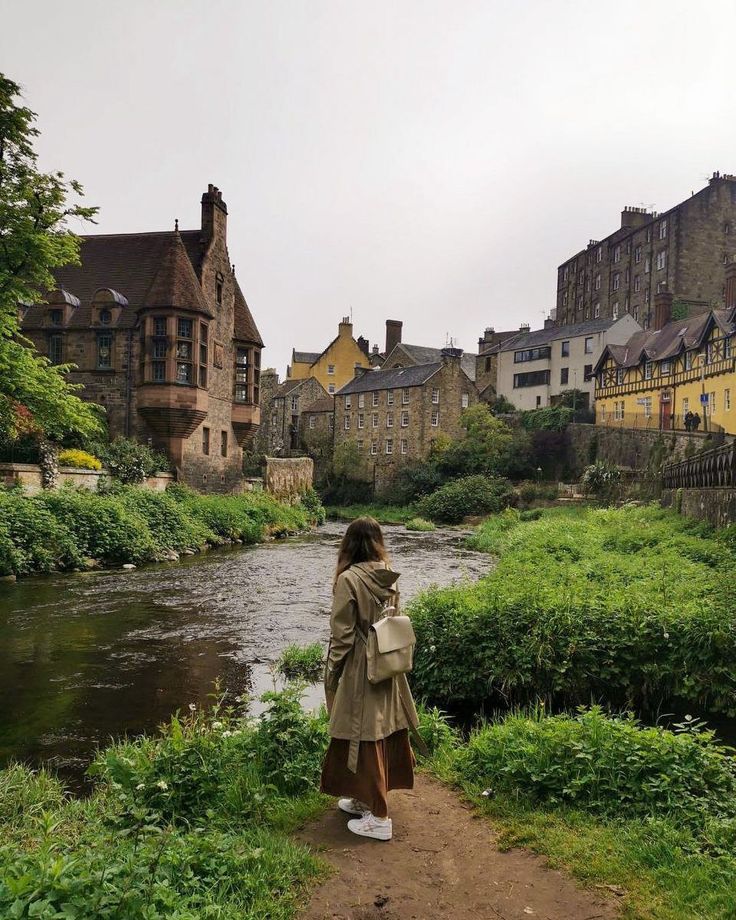 a woman standing on a path next to a river in the middle of a town