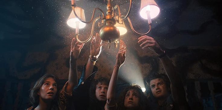 a group of people standing under a chandelier holding up their hands in the air