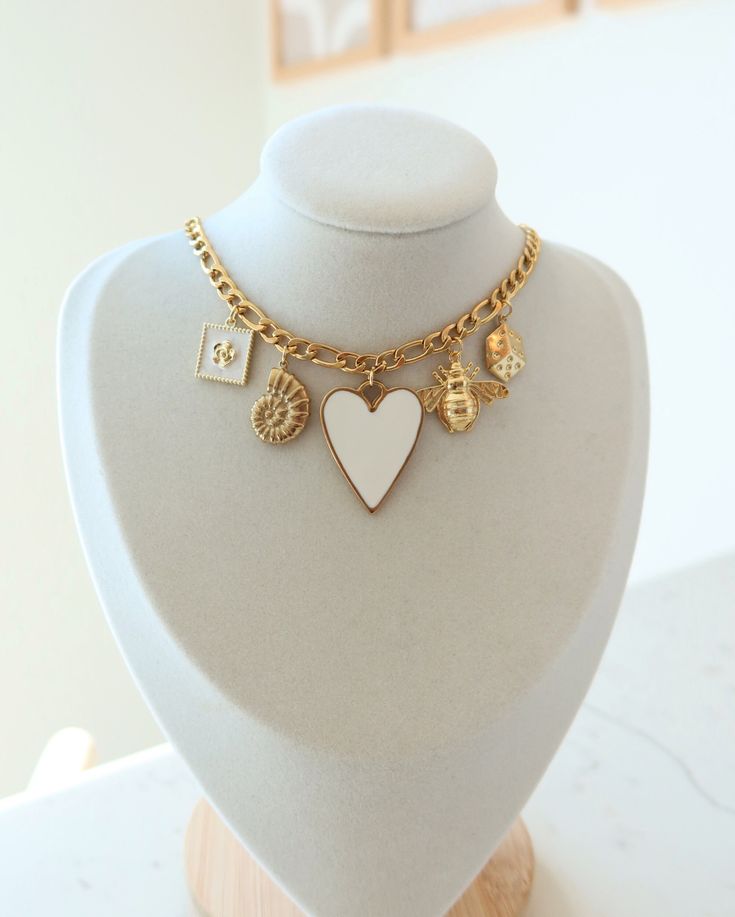 A charm necklace curated with five charms. The perfect gift for the person who loves a statement piece. Set against gold plated Figaro necklace with a 18K gold plated toggle clasp Featuring a large white heart pendant, bee charm, dice charm, shell charm and gold flower with white enamel charm. White Necklaces With Logo Charm For Gift, White Necklaces With Logo Charm As Gift, White Necklace With Logo Charm For Gift, White Necklace With Logo Charm As Gift, Gold-tone Pendant Charm Necklace With Heart Charm, White Jewelry With Logo Charm For Gift, White Jewelry With Logo Charm As A Gift, Everyday White Dangling Charms, White Dangling Pendant Charms