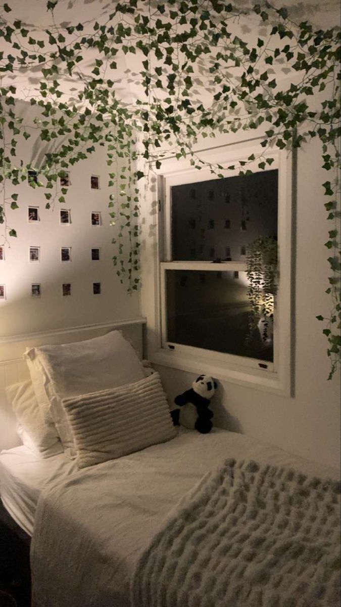 a bed with white sheets and pillows in a room decorated with green ivy vines hanging from the ceiling