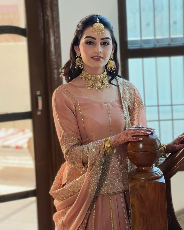 a woman in a pink outfit standing next to a wooden railing and looking at the camera