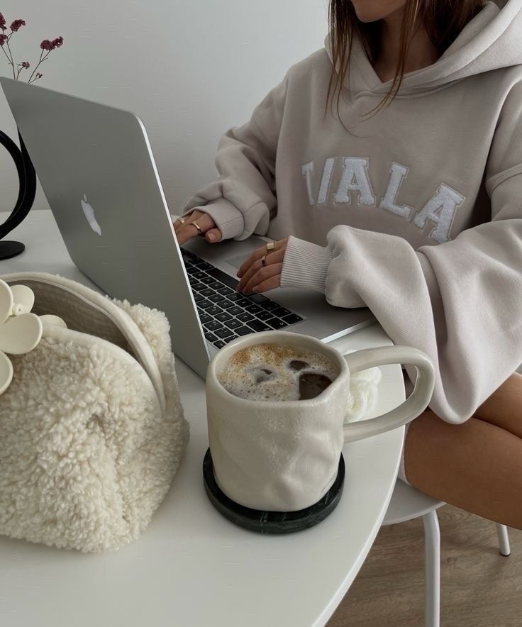 a woman sitting at a table with a laptop and cup of coffee in front of her