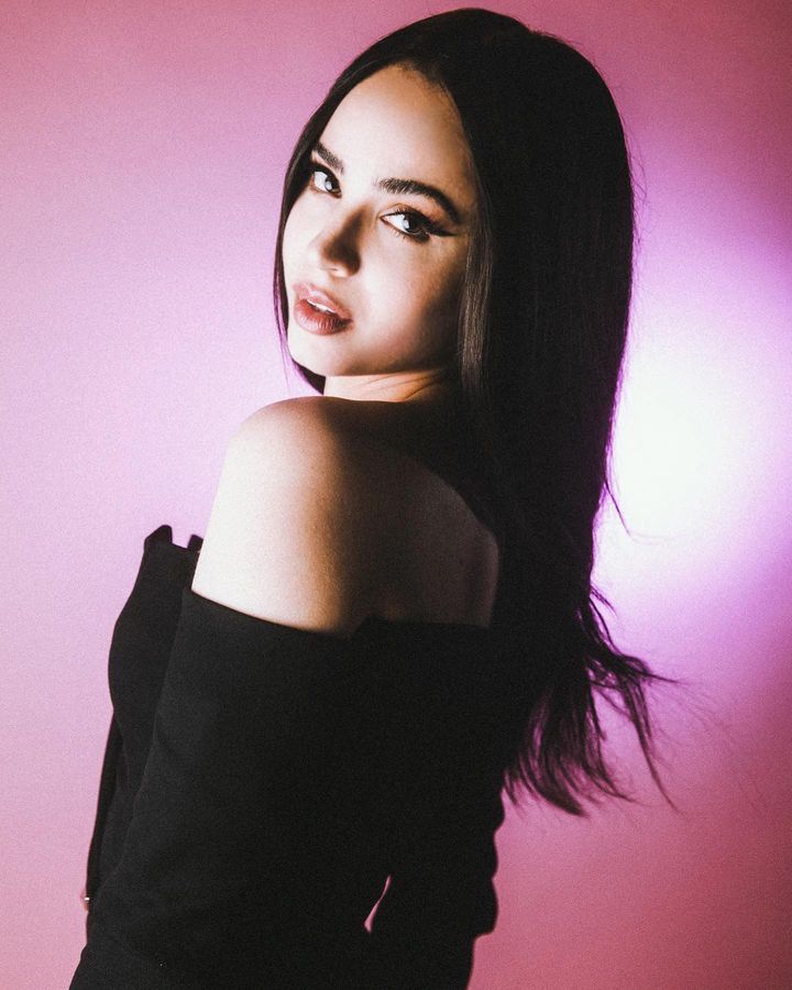 a woman with long black hair posing for a photo in front of a pink background