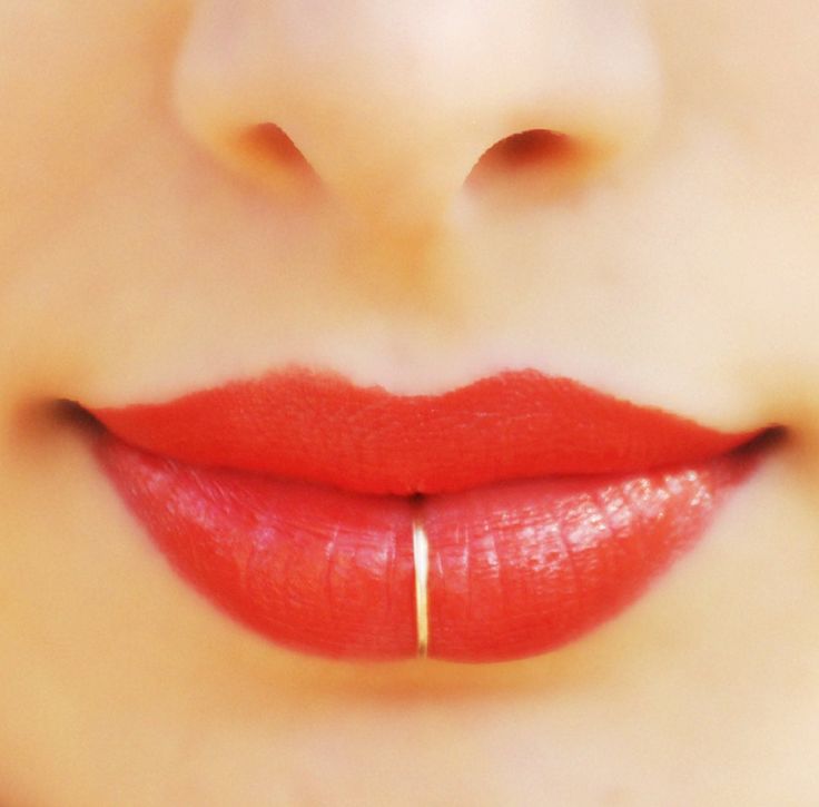 a woman's lips with red lipstick and gold hoop on the tip of her nose