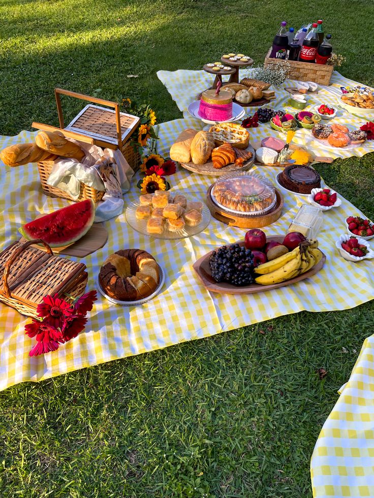 an outdoor picnic is set up in the grass with food on it, including bread and fruit