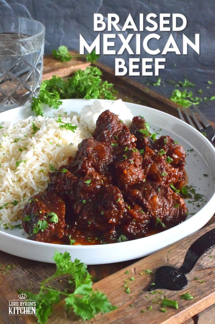 a white plate topped with meat and rice next to a glass of water on a wooden table