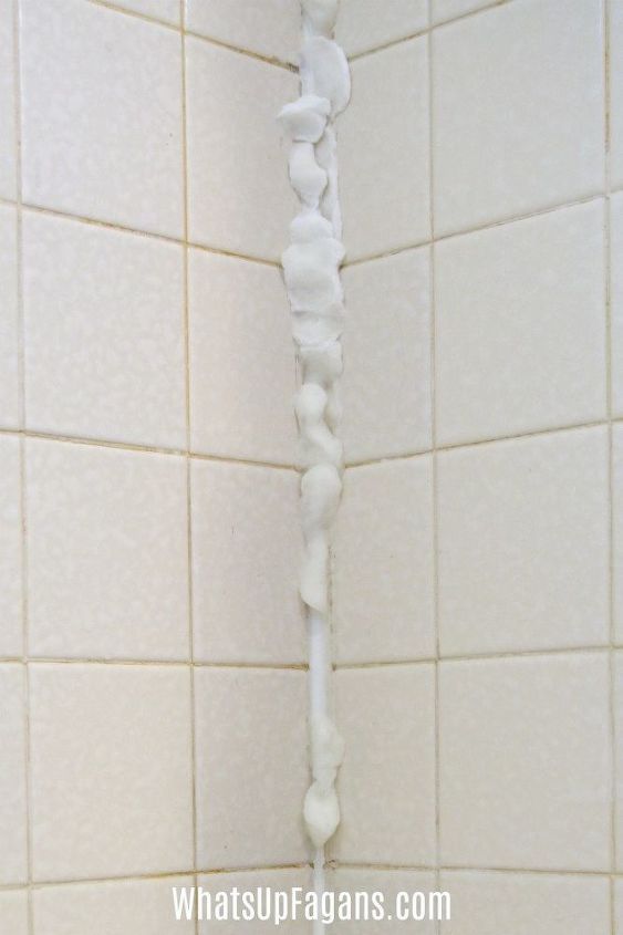 a white shower head in the corner of a tiled wall with water coming from it