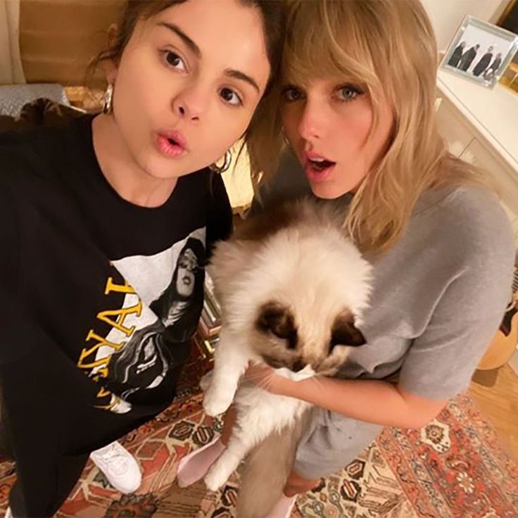 two women pose with their cat on the bed