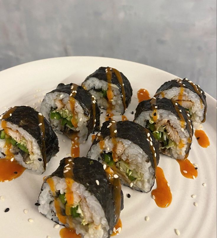 sushi rolls on a white plate with sauce drizzled over them