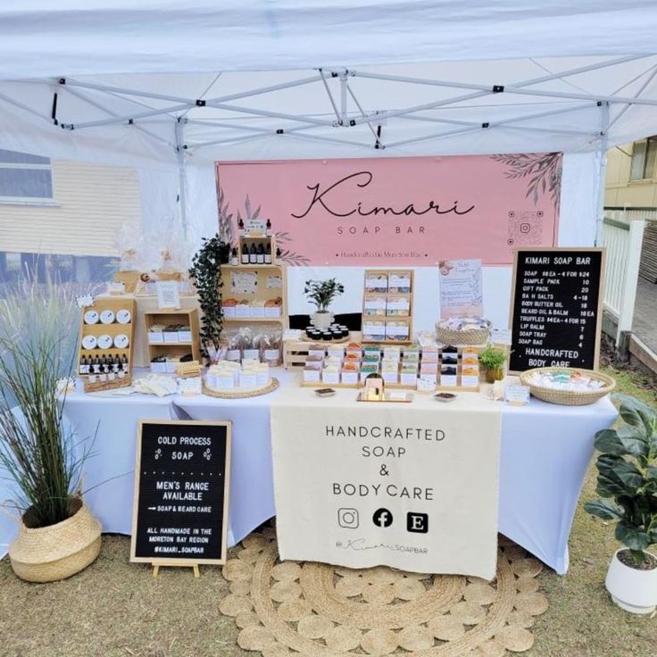 a table topped with lots of food under a white and pink sign that says handcrafted soap