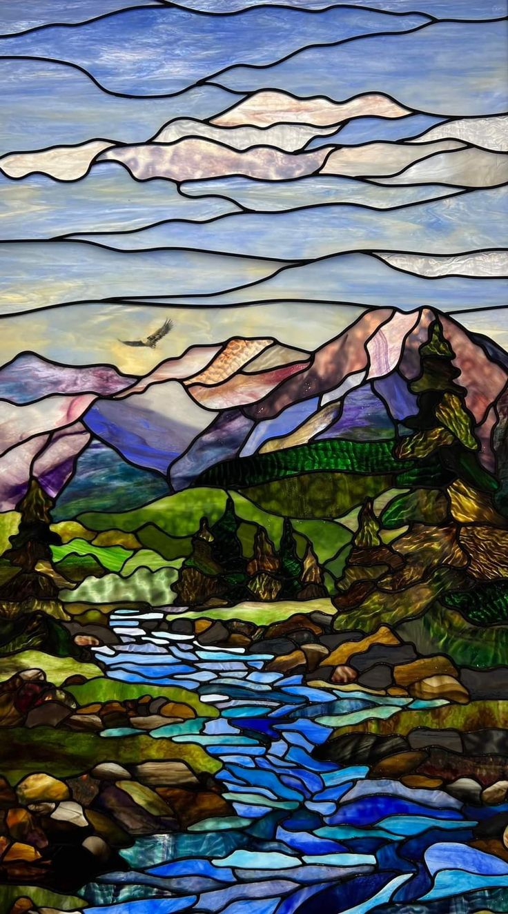 a stained glass window with mountains and water in the background, as well as clouds