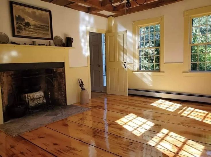 an empty living room with wood floors and fireplace in the center, sunlight streaming through windows