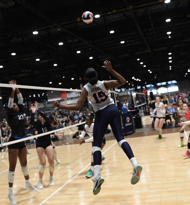 a group of women playing volleyball on a court with people watching from the sidelines