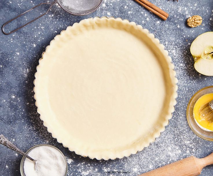 an uncooked pie crust next to other ingredients on a blue surface with wooden spoons