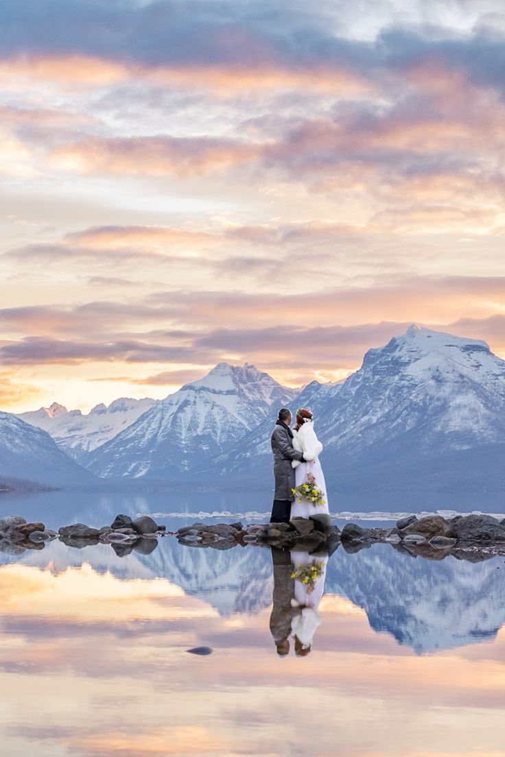 a bride and groom standing on rocks in front of water with mountains in the background