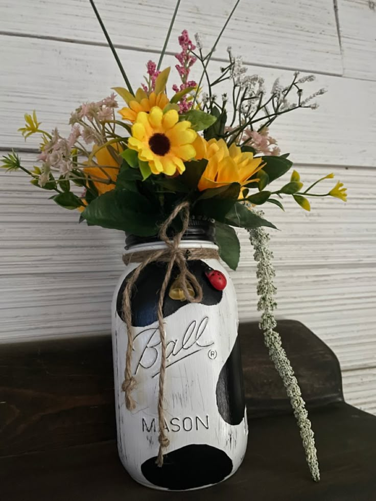 a mason jar with sunflowers and daisies tied to it