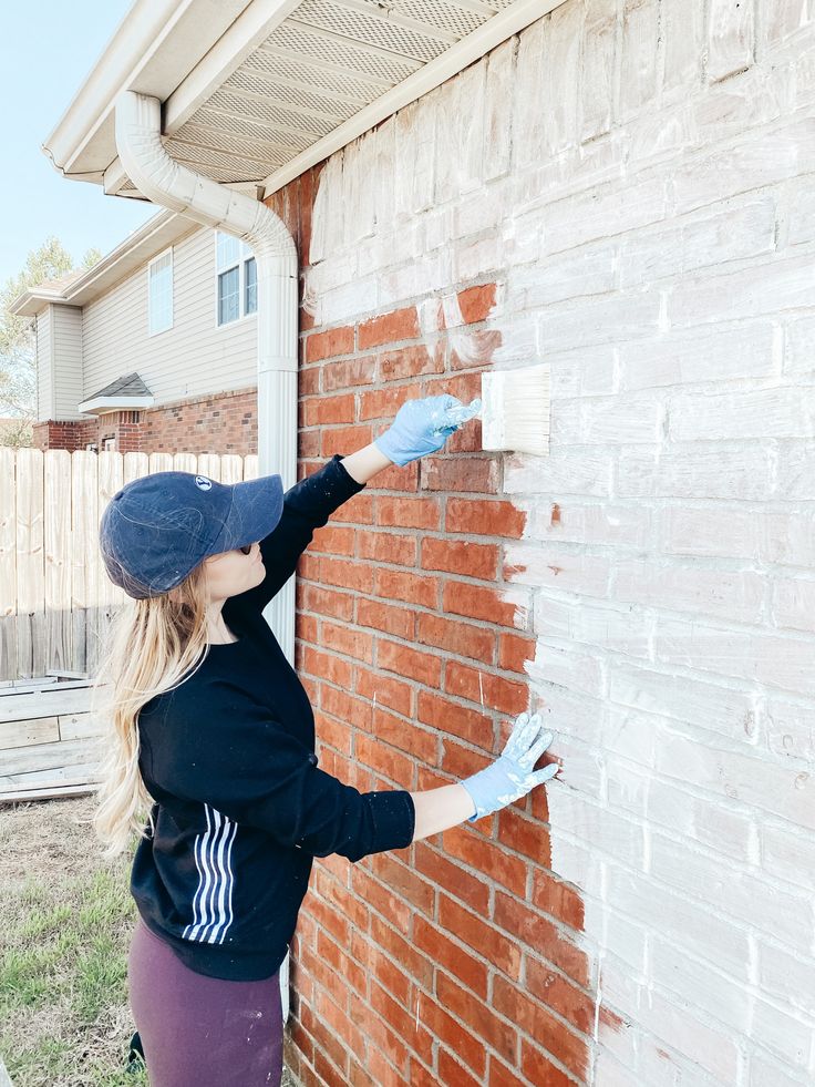 a woman is painting the side of a brick building with white paint and blue gloves