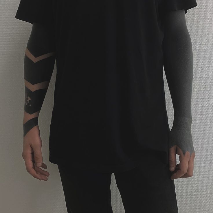 a man with tattoos on his arm standing in front of a white wall and wearing a black t - shirt