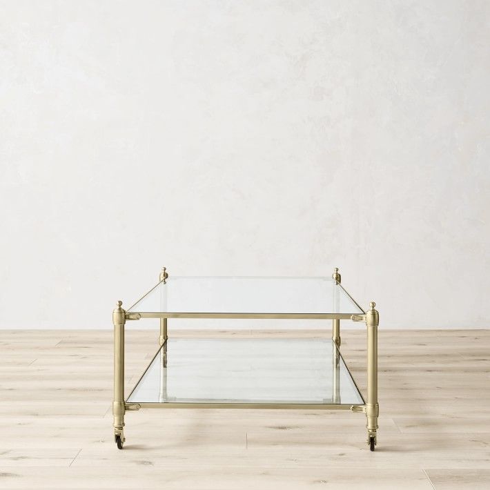 a glass and brass coffee table sitting on top of a hard wood floor in front of a white wall