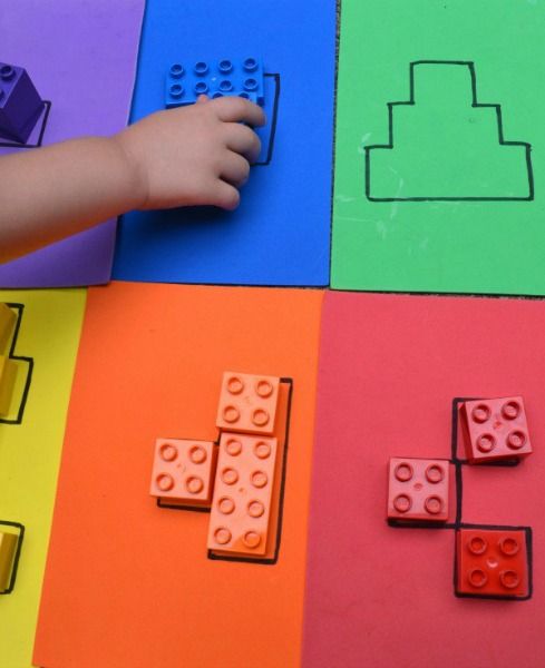 a child's hand is placing lego blocks on top of the colored paper squares