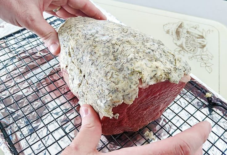 two hands are holding up a piece of meat on a cooling rack