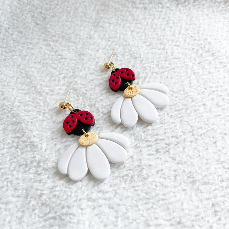 two ladybug earrings on top of each other in white and red with gold accents