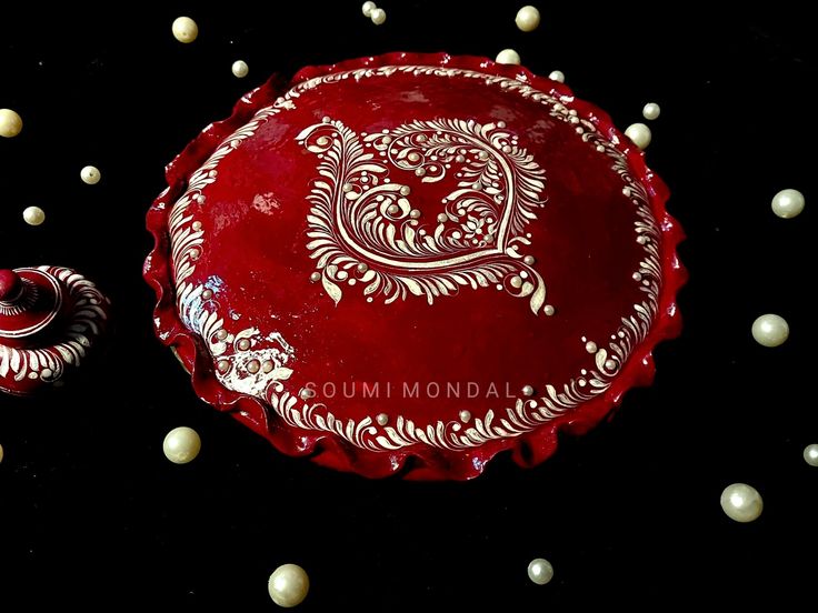 a red plate with white designs on it sitting next to two candles and some pearls