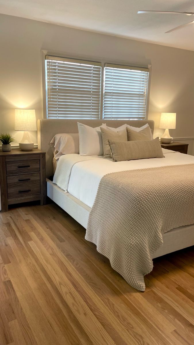 a large bed sitting next to two lamps on top of a hard wood floored bedroom