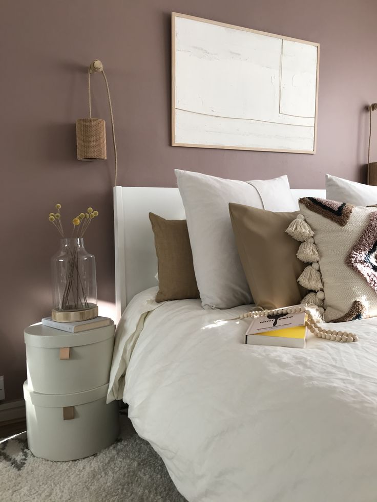 a white bed topped with lots of pillows next to a painting on the wall above it