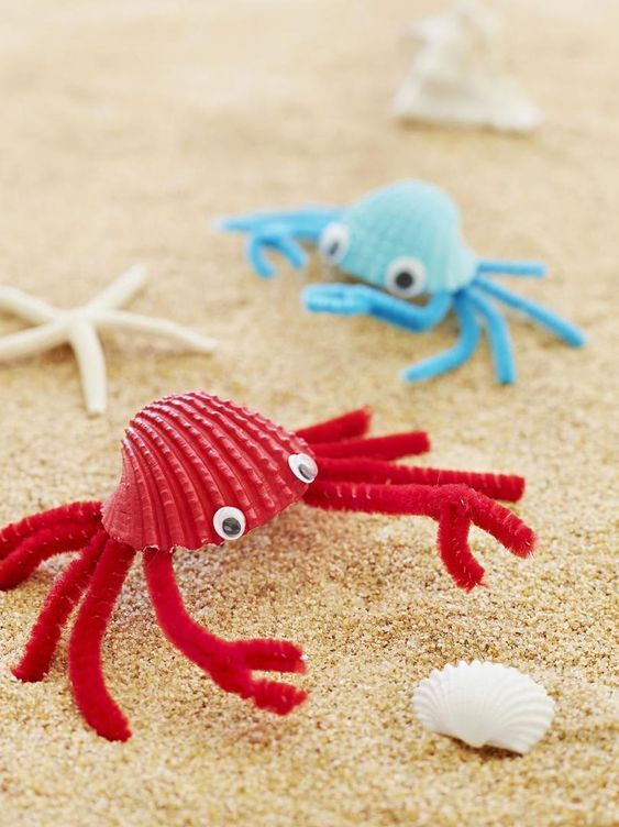 two red and one blue sea animals on the sand with shells in front of them