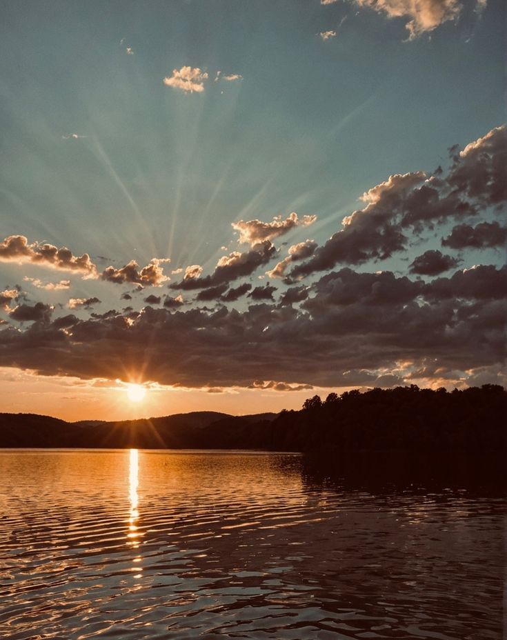 the sun is setting over water with clouds in the sky