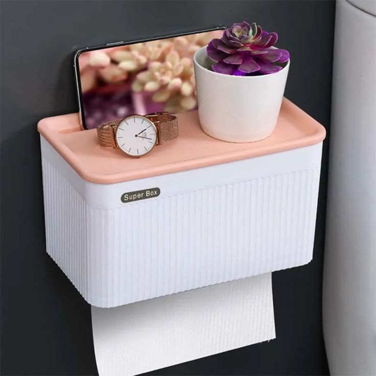 a white toilet paper holder with a pink and white watch on it next to a plant