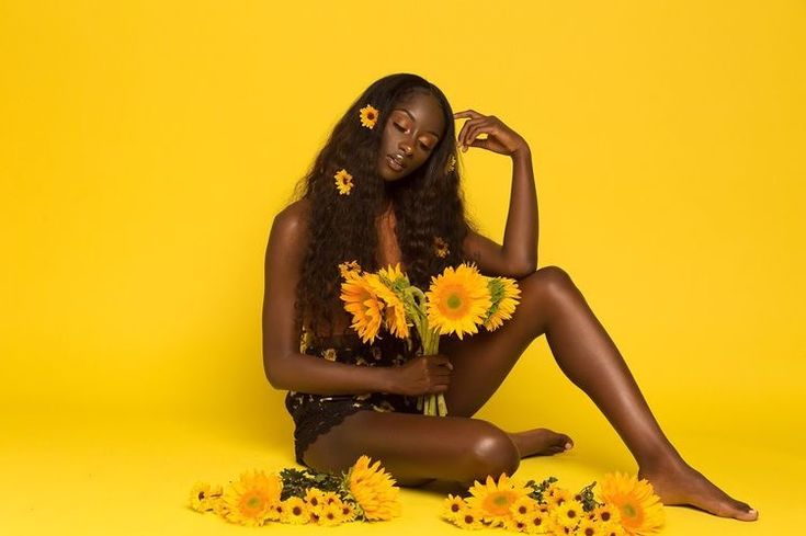 a woman sitting on the ground with sunflowers in her lap and one arm behind her head