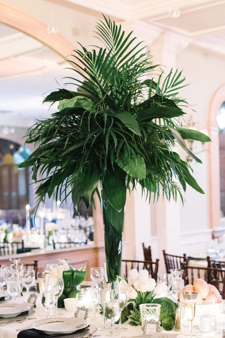 a tall plant is in the center of a table set for an elegant wedding reception