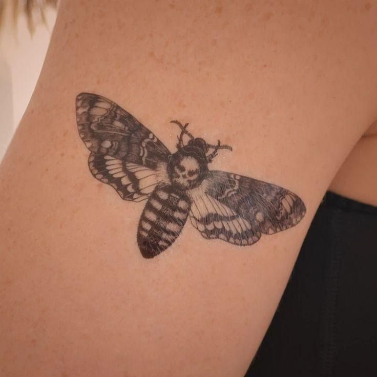 a small moth tattoo on the back of a woman's right arm and shoulder