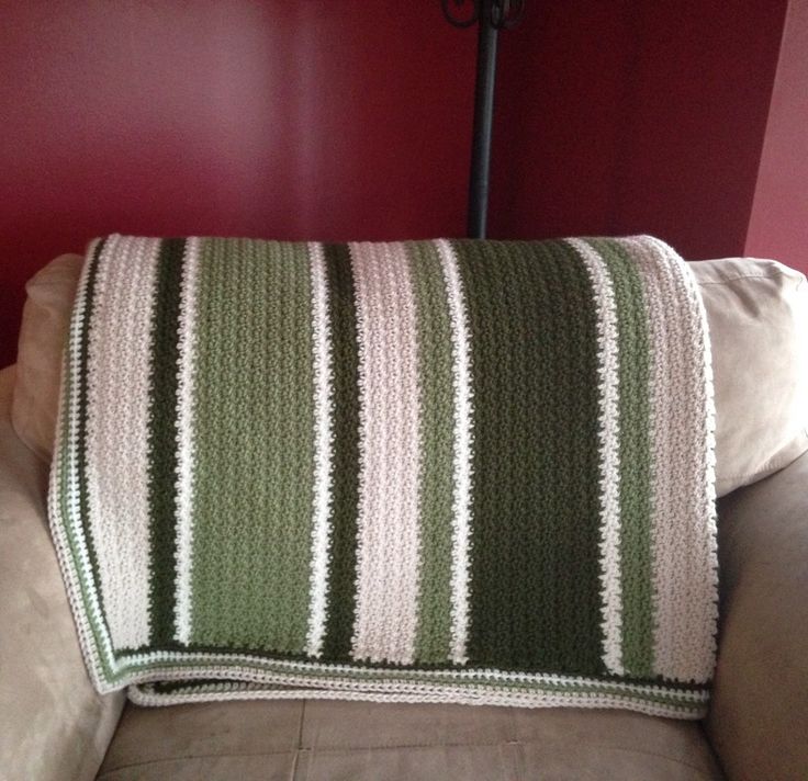 a couch with a green and white striped blanket on it's back, next to a red wall