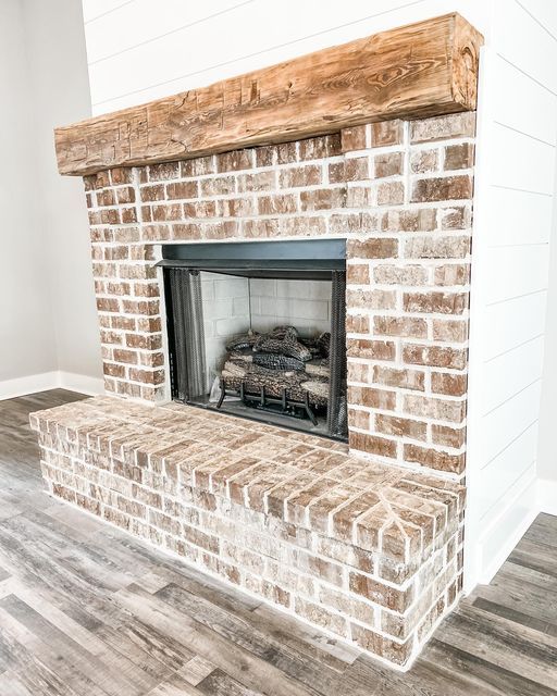 a brick fireplace in a white room with wood flooring and a wooden mantel