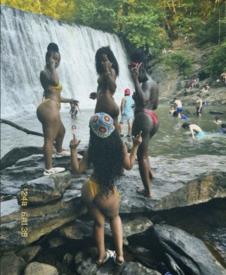 some people are standing in the water near a waterfall and having fun with each other