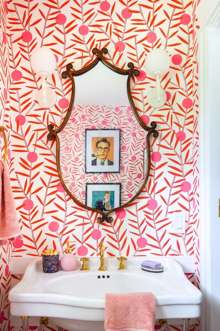 a bathroom with pink and orange wallpaper, gold faucet, white sink and mirror