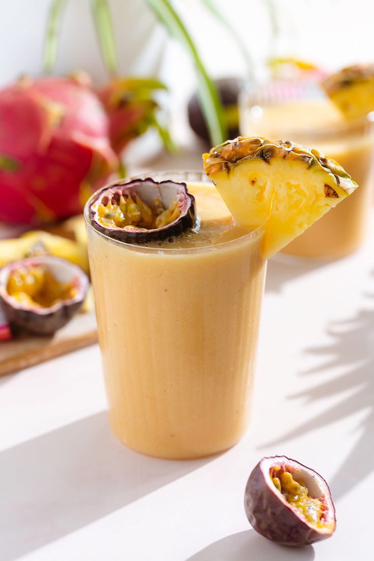 two glasses filled with smoothie and fruit on a table next to some other fruits