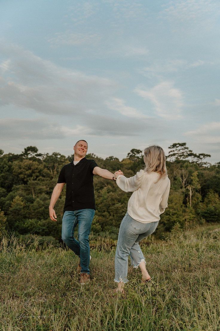 a man and woman holding hands while standing on top of a grass covered field with trees in the background