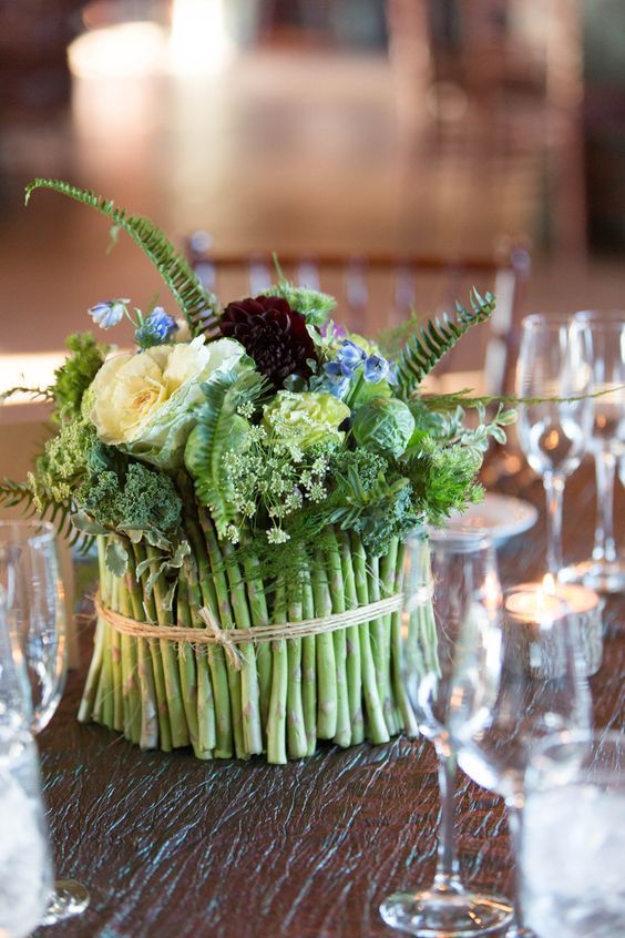 an arrangement of flowers and greenery in a basket on a table with wine glasses