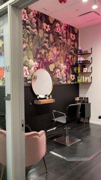 a salon with pink chairs and floral wallpaper on the walls, in front of a mirror