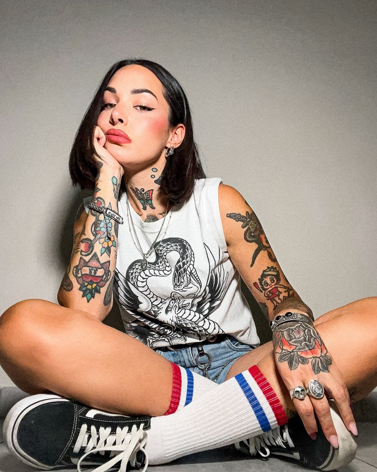 a woman sitting on the floor with her legs crossed and tattoos on her arms,