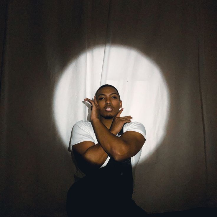 a man sitting in front of a white curtain with his hands on his face and arms crossed