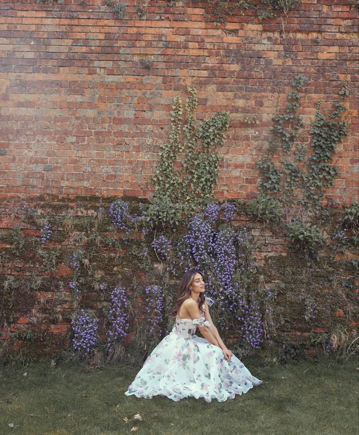 a woman sitting in front of a brick wall wearing a dress with flowers on it