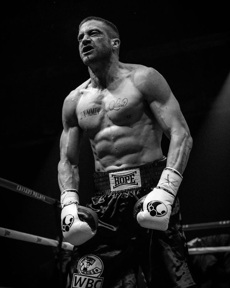 a shirtless man standing next to a boxing ring with his hands on his hips