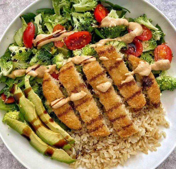 a white plate topped with rice, chicken and veggies next to a salad