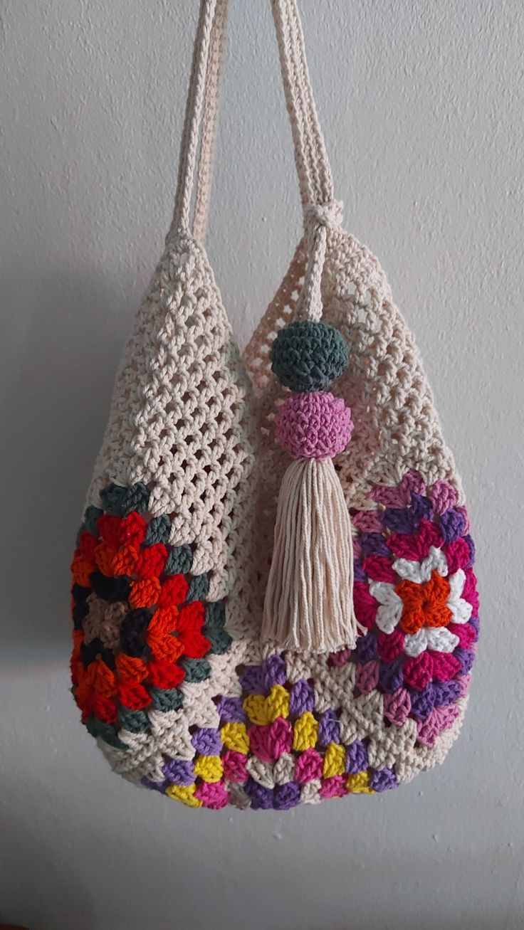 a crocheted bag hanging from a hook on a wall with flowers and tassels