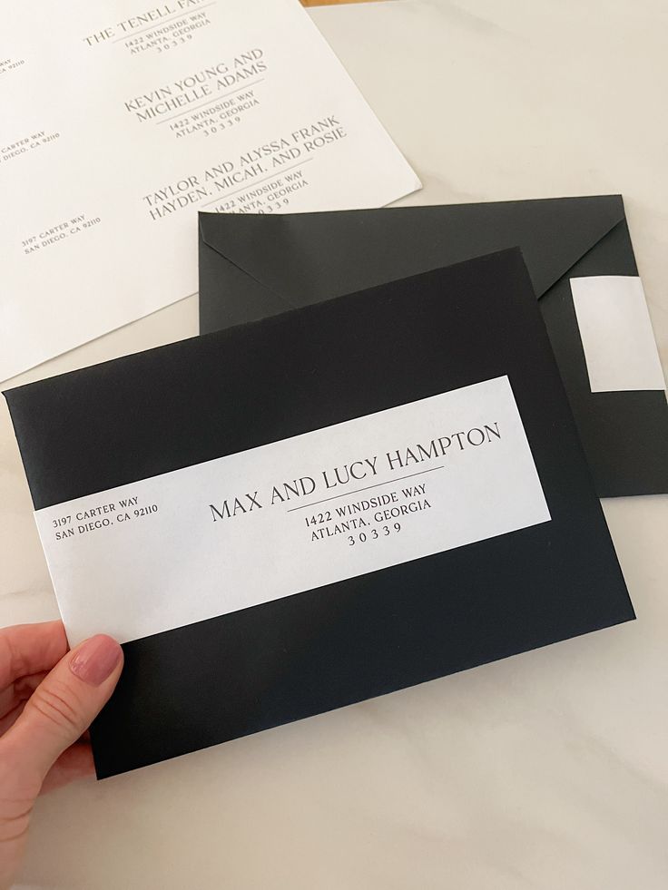 a person is holding up some black and white envelopes that are on top of a table